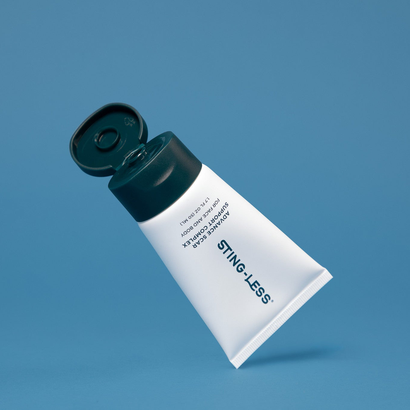 A squeeze tube of STING-LESS facial pain relief cream, shown tilted on a solid blue background with its cap open.