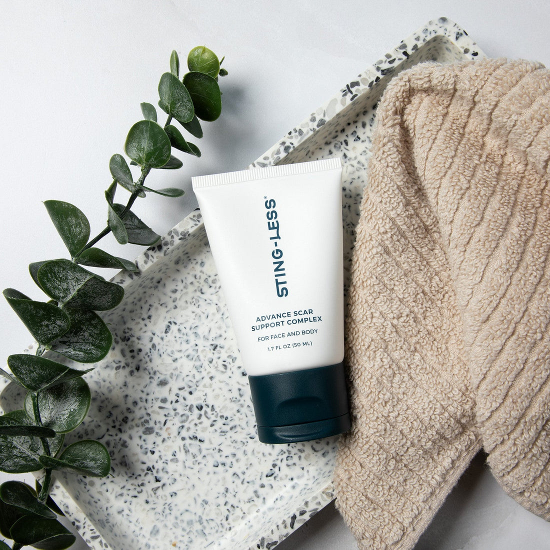 Sting-Less Advance Scar Support Complex tube on a terrazzo tray with eucalyptus and a towel