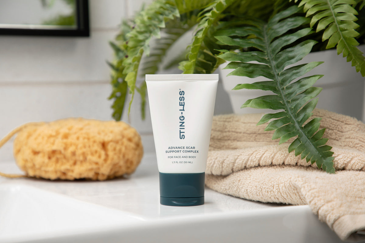 Sting-Less Scar Support Complex tube beside a fern, a sponge and a folded towel
