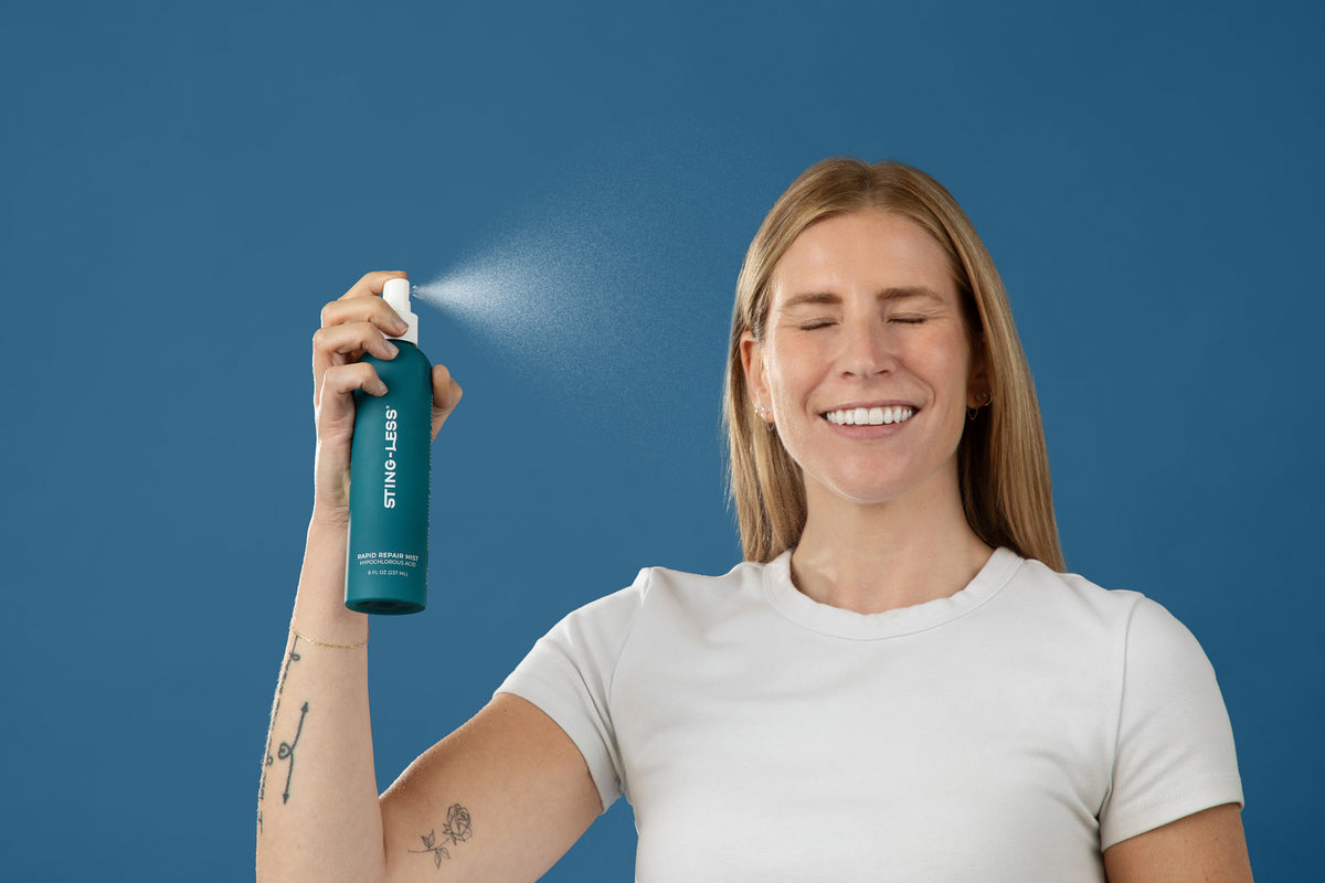 Smiling woman spraying Sting-Less Rapid Repair Mist toward her face against a blue background