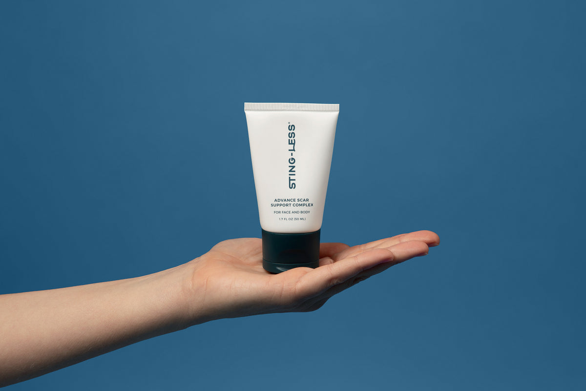 Sting-Less Scar Gel tube resting on an open palm against a blue background